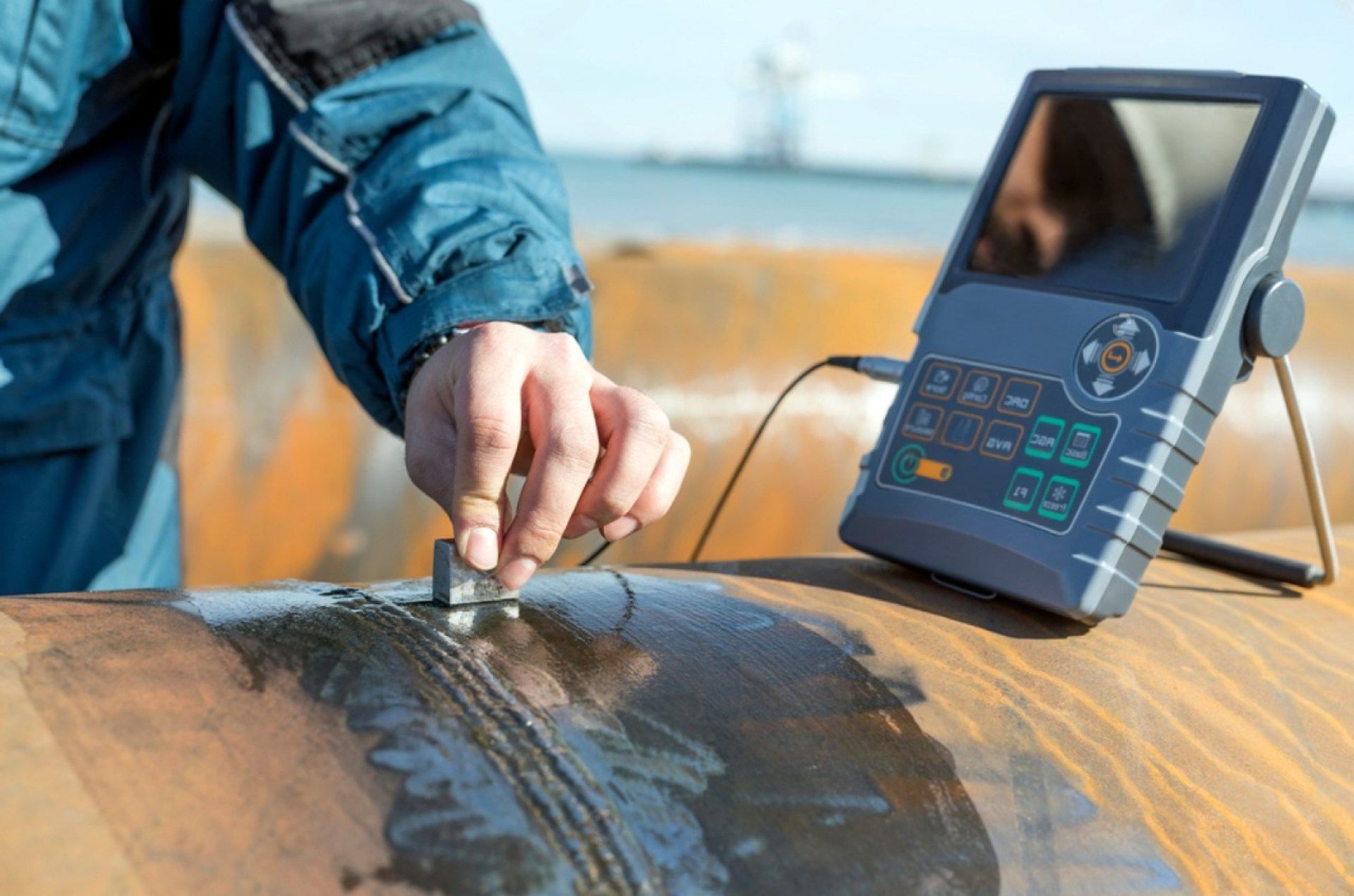 Ein Mann misst mit einem Ultraschallgerät die Dicke eines Rohrs.