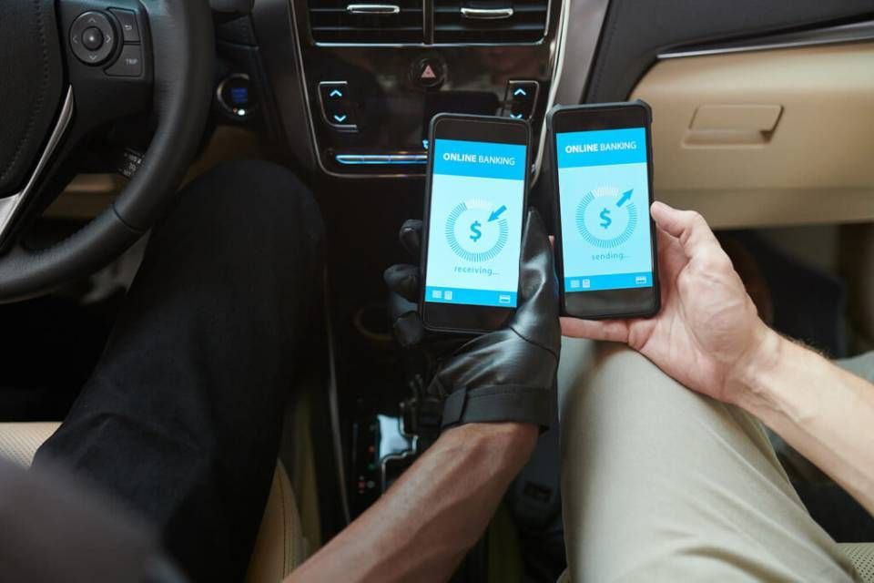 Zwei Personen in einem Auto vergleichen die Bildschirme von Zahlungs-Apps auf ihren Smartphones.