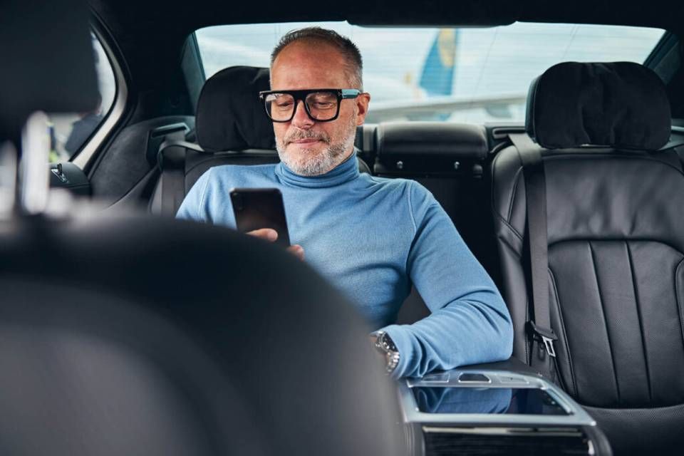Mann in blauem Pullover benutzt Smartphone im Innenraum eines Autos