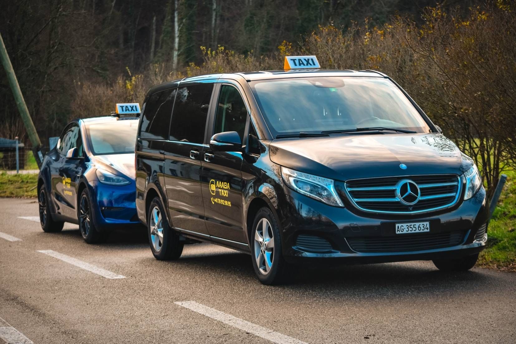 Ein schwarzer Mercedes-Transporter zieht einen blauen Rennwagen über die Strasse; beide Fahrzeuge tragen Startnummern auf dem Dach.