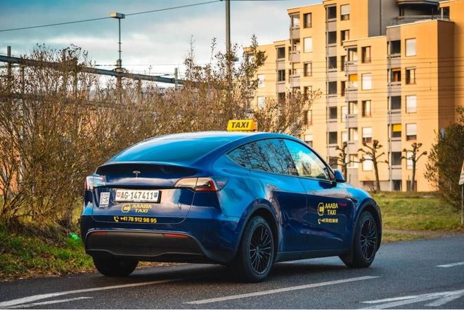 Ein blaues Taxi parkt in der Abenddämmerung am Strassenrand in der Nähe von Wohnhäusern.