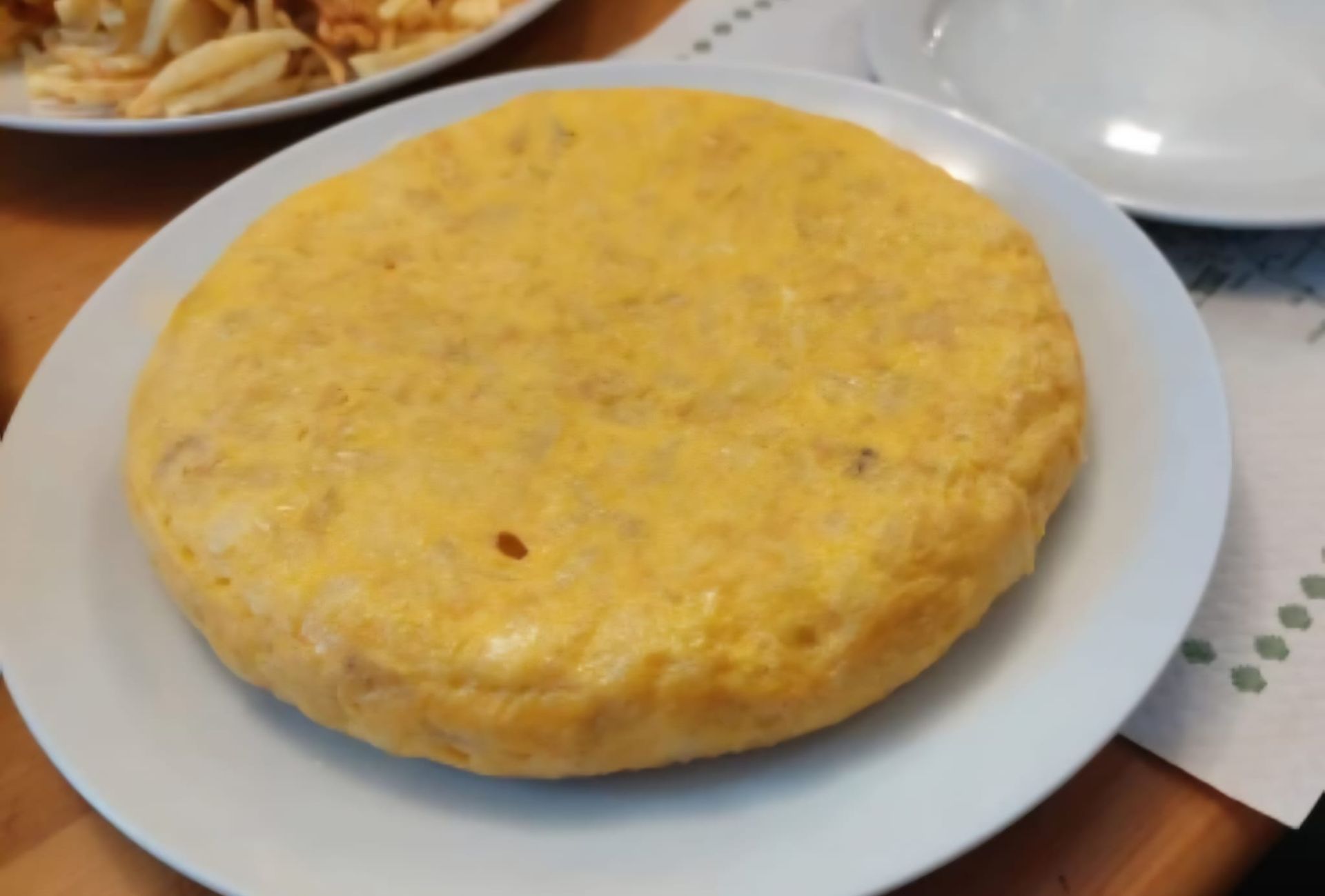 Tortilla española sobre un plato blanco, amarilla y redonda.