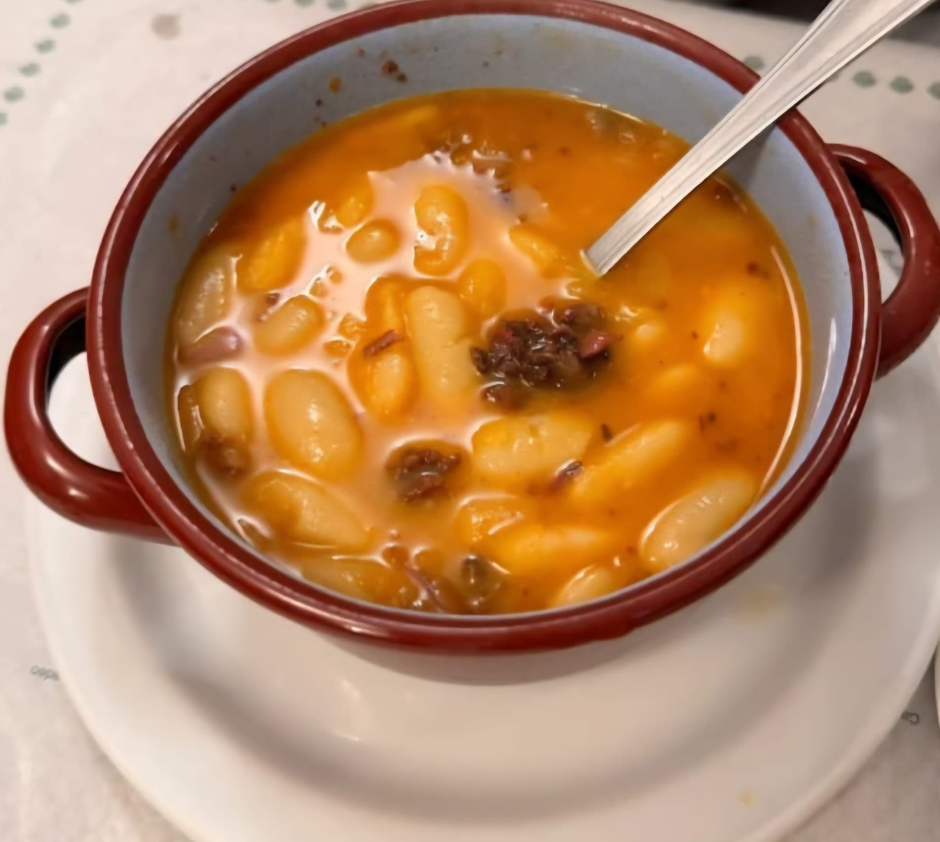 Plato de estofado de alubias blancas con carne, servido en un rústico cuenco marrón con asas.