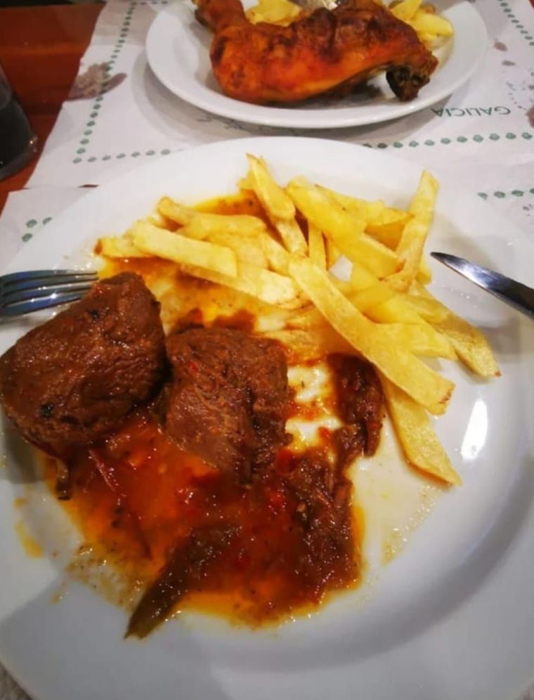 Plato de comida: carne con salsa y patatas fritas. Muslo de pollo en un plato al fondo.