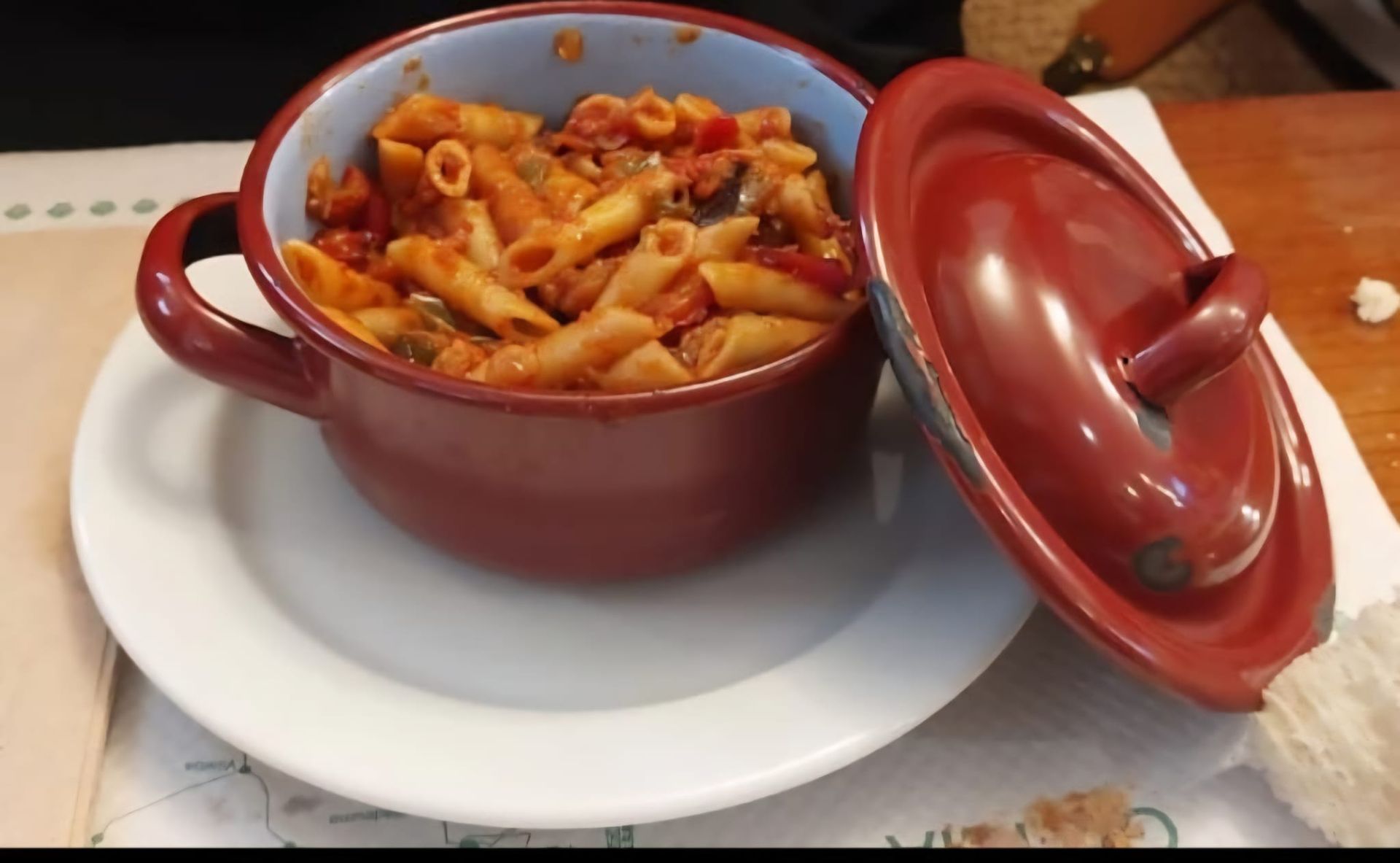 Pasta en una olla de cerámica roja sin tapa, colocada sobre un plato blanco.