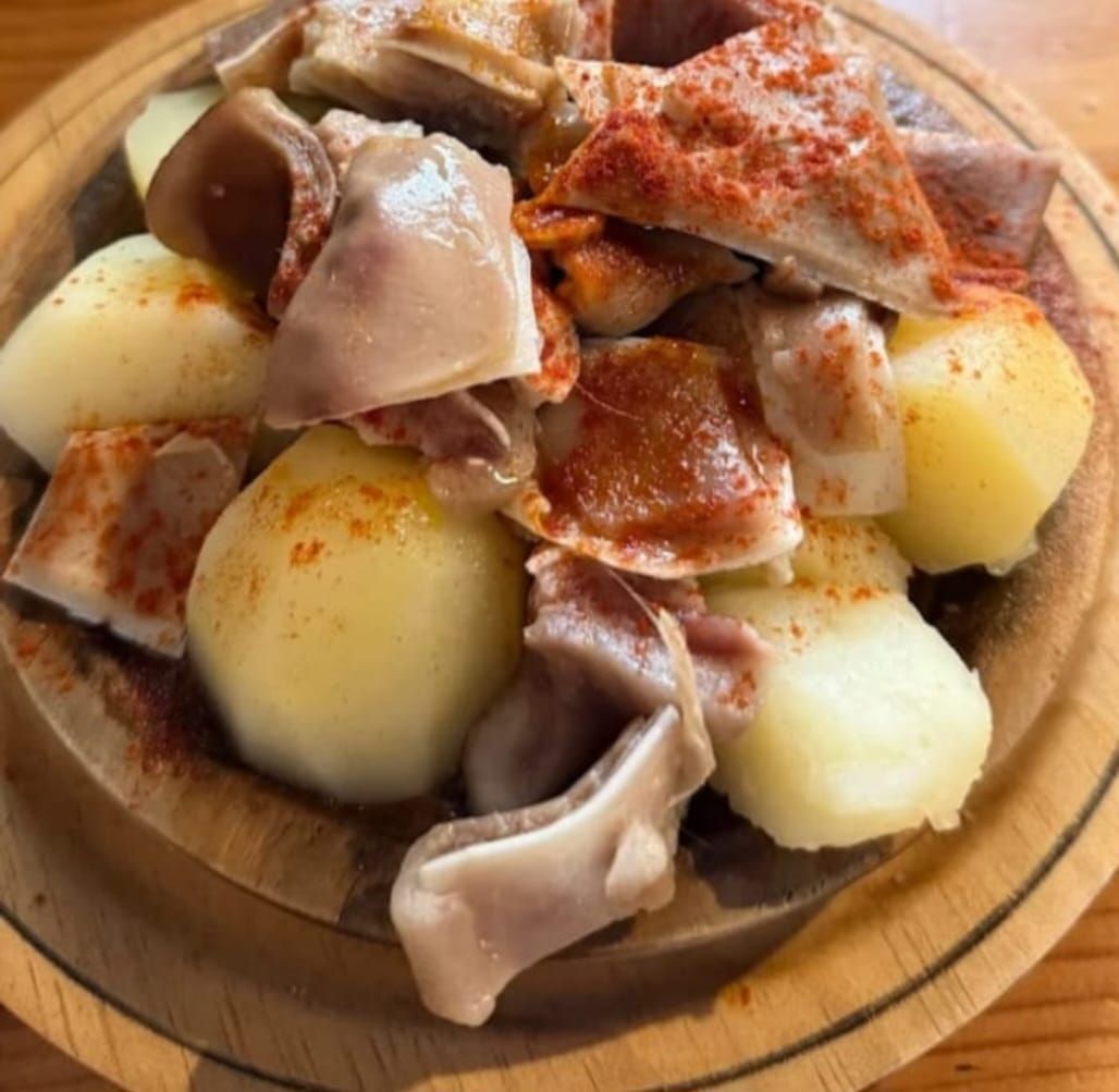 Patatas hervidas y carne espolvoreadas con pimentón rojo en un bol de madera.