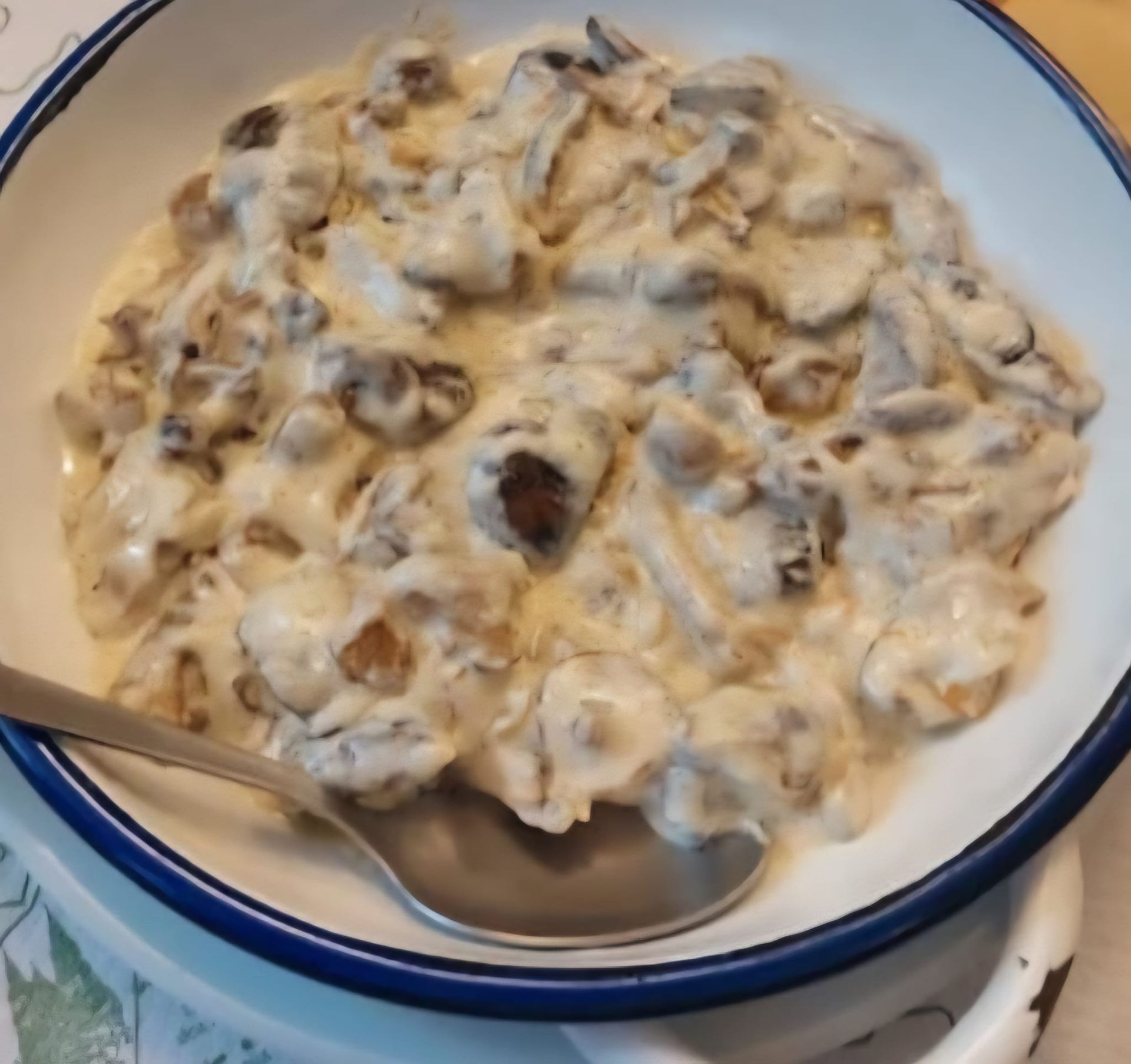 Plato cremoso de champiñones en un tazón blanco con borde azul, con una cuchara visible.