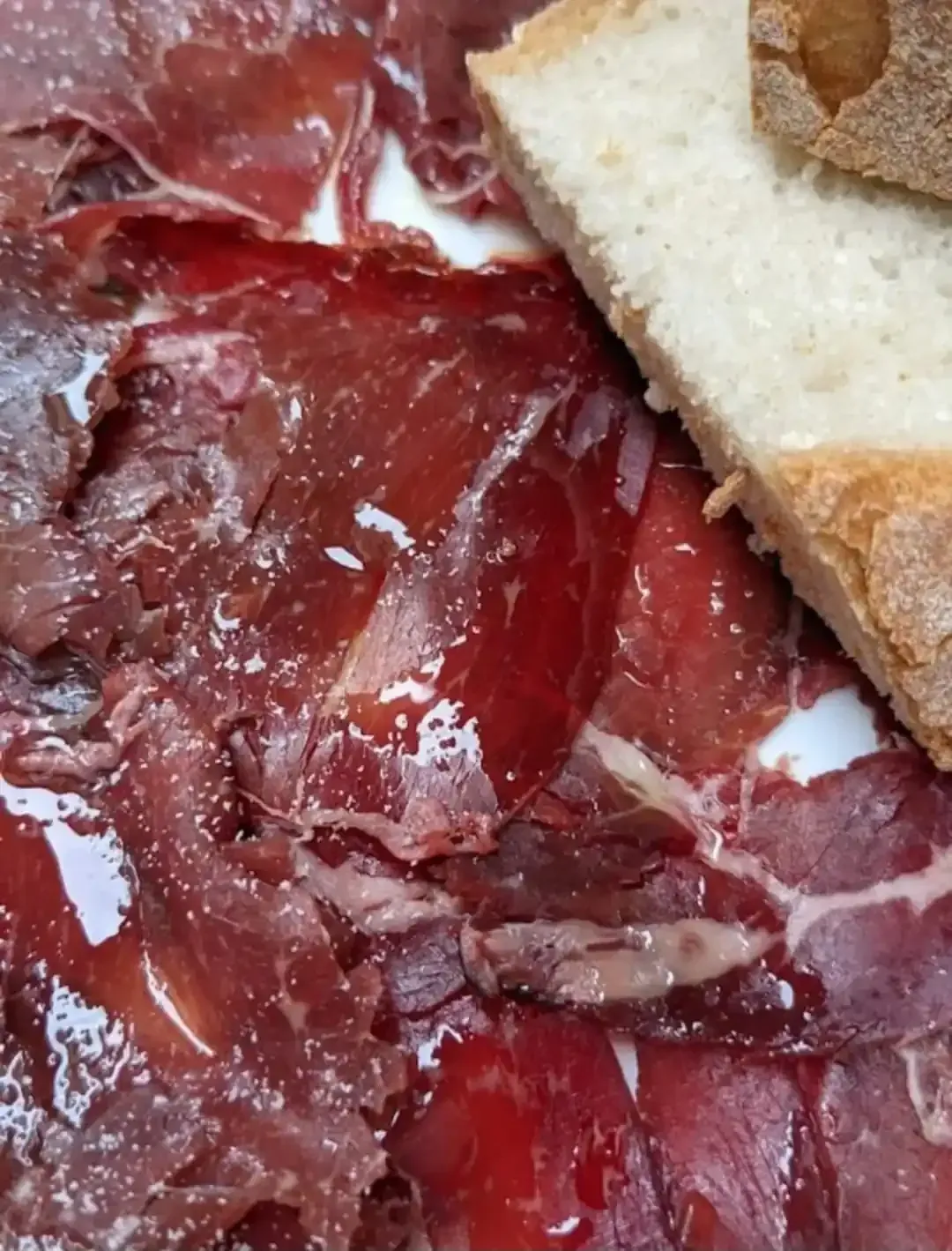 Finas lonchas de embutido curado, de color marrón rojizo, con una rebanada de pan blanco.