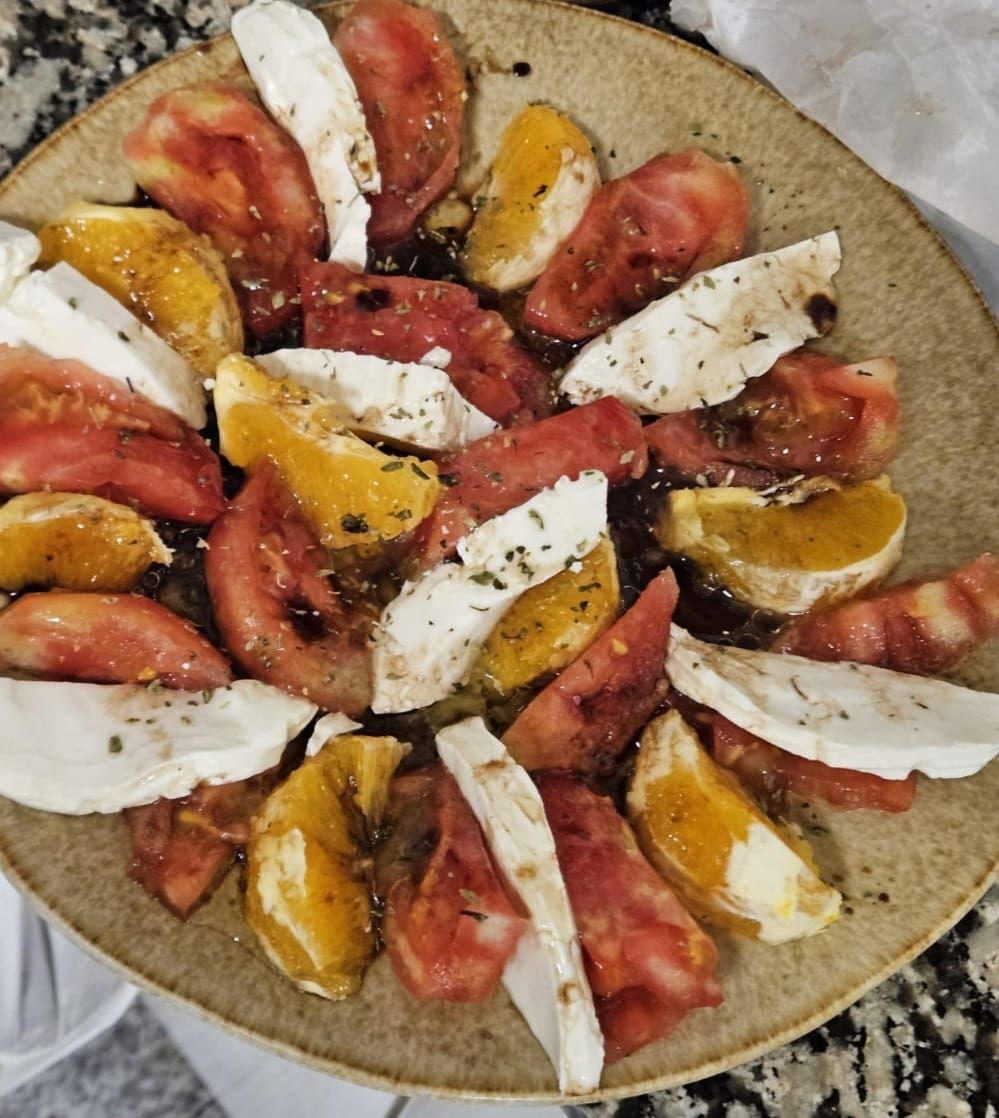 Ensalada con rodajas de tomate, naranja y mozzarella, rociada con aderezo en un plato.