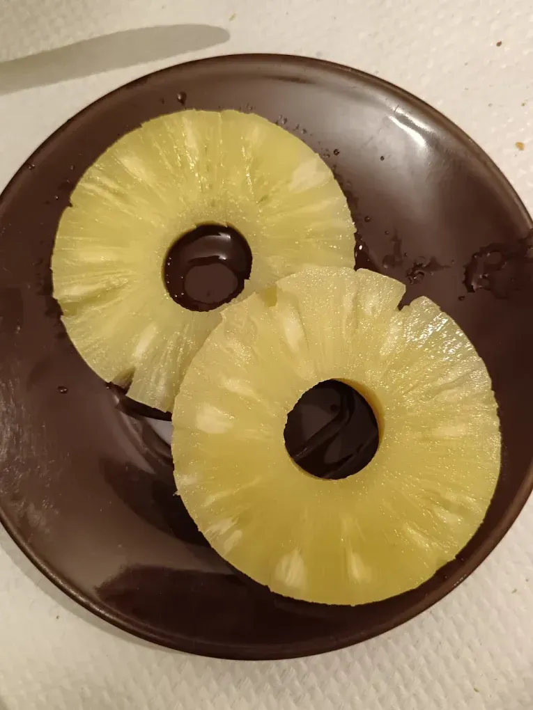 Dos rodajas de piña sobre un plato marrón. Fruta amarilla, plato marrón oscuro.