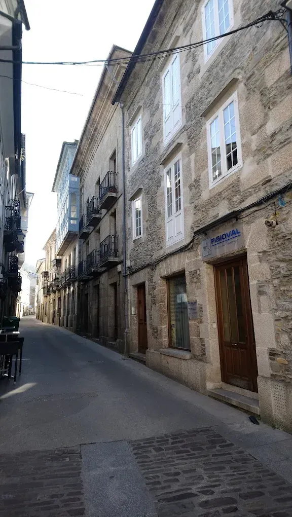 Calle estrecha y empedrada flanqueada por antiguos edificios de piedra, algunos con balcones y tiendas