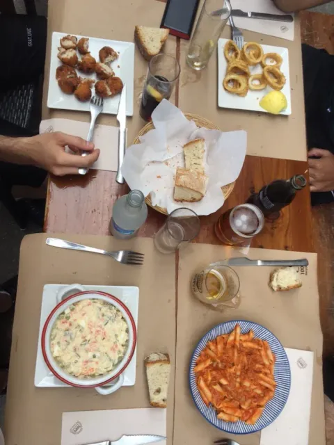 Mesa con varios platos de comida: fritos, pasta, ensalada y pan.