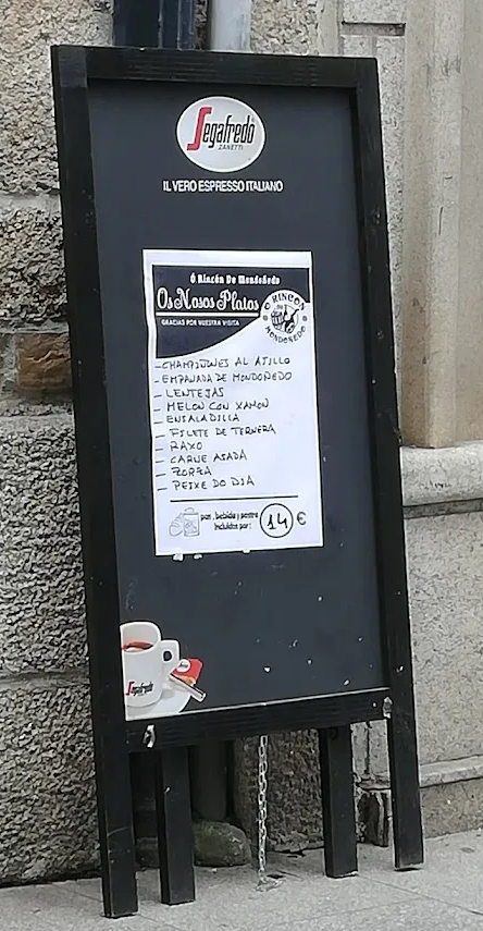 Un cartel de pizarra negra apoyado contra una pared de piedra, con un menú adjunto.