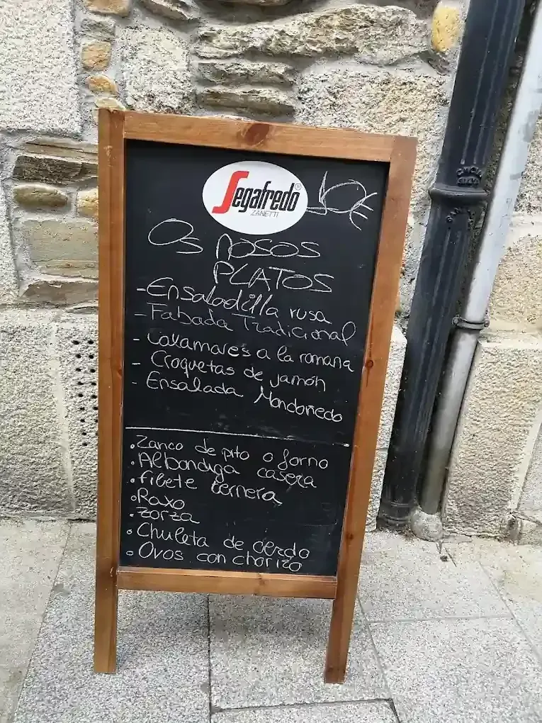 Menú de pizarra de madera en la acera, con la lista de "Os Pratos" y sus platos y bebidas en español.