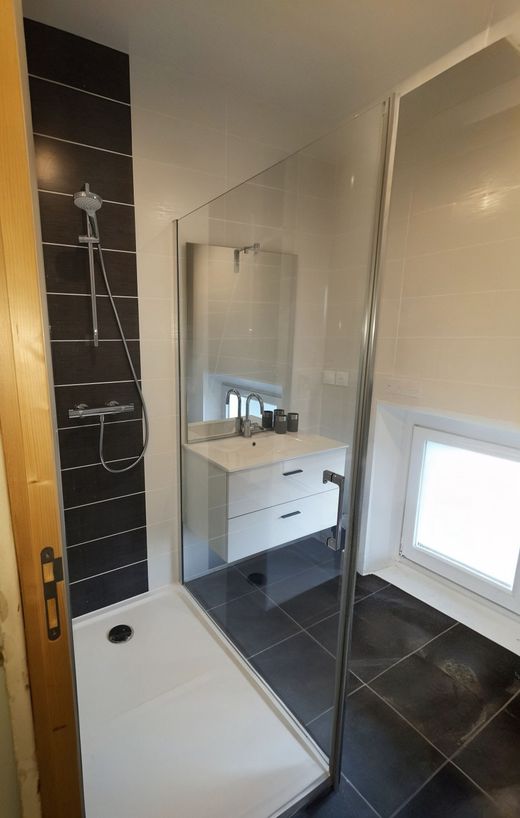 Salle de bains moderne avec meuble lavabo rouge, lavabo blanc, miroir rond et murs carrelés en noir et blanc