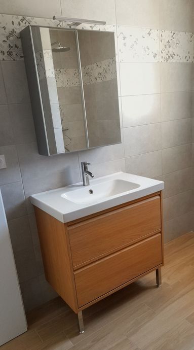 Meuble lavabo moderne avec lavabo blanc, armoire en bois et étagères ouvertes contre des murs carrelés.