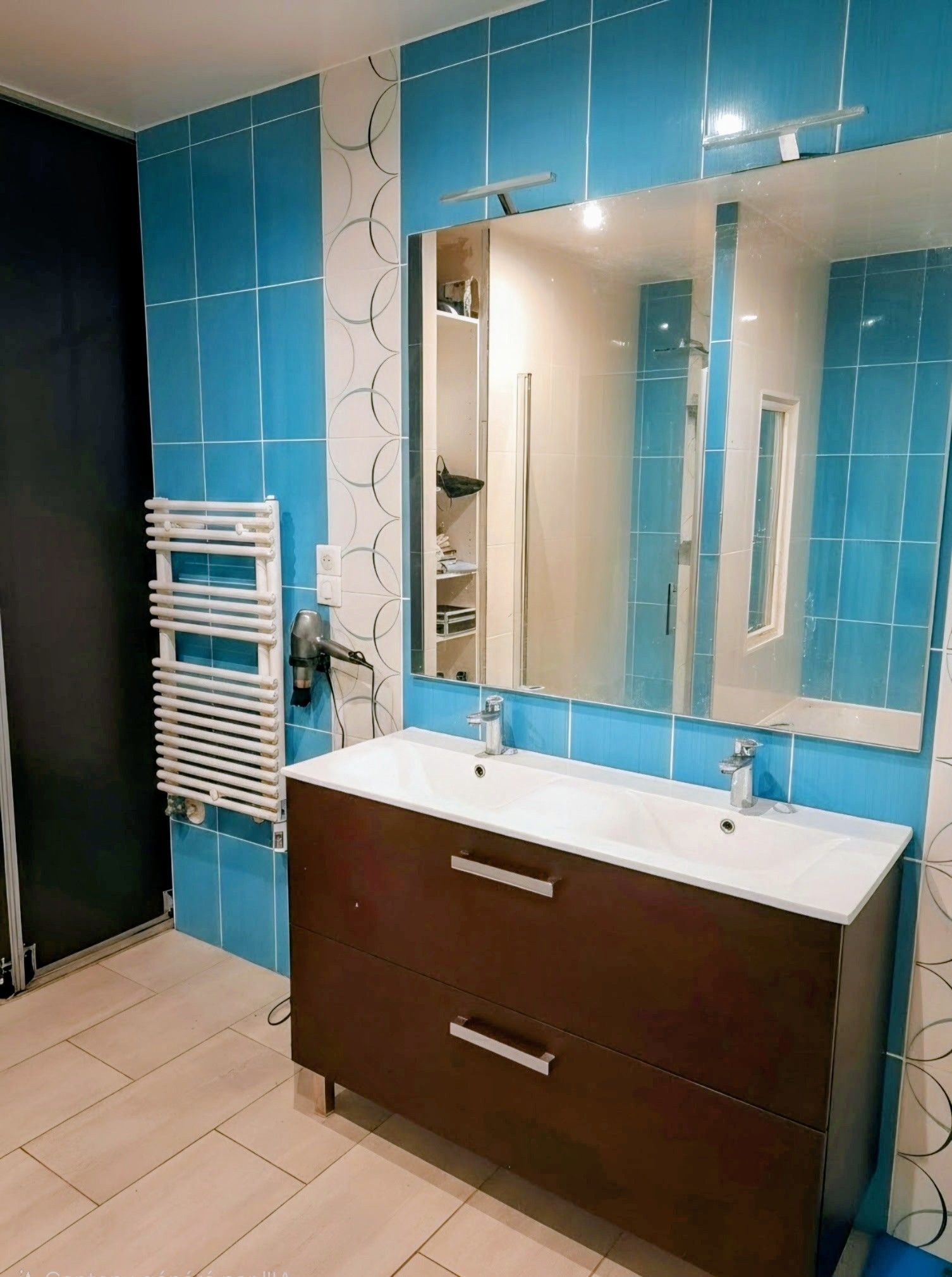 Salle de bains moderne avec murs carrelés bleus, grand miroir et meuble lavabo foncé.