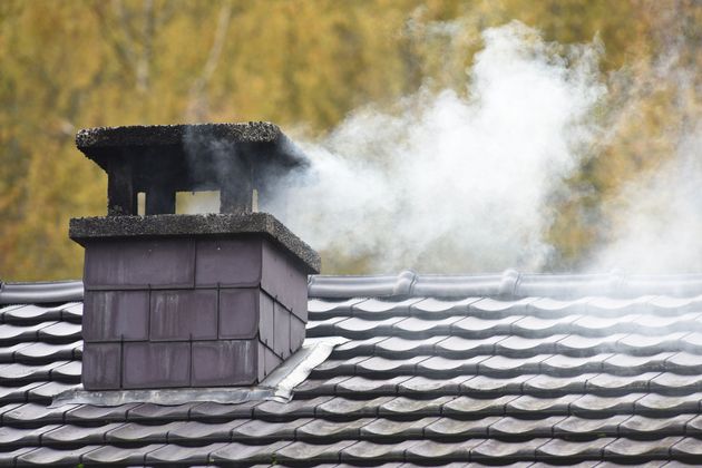 Cheminée noire sur le toit, dégageant une fumée blanche sur un fond flou.