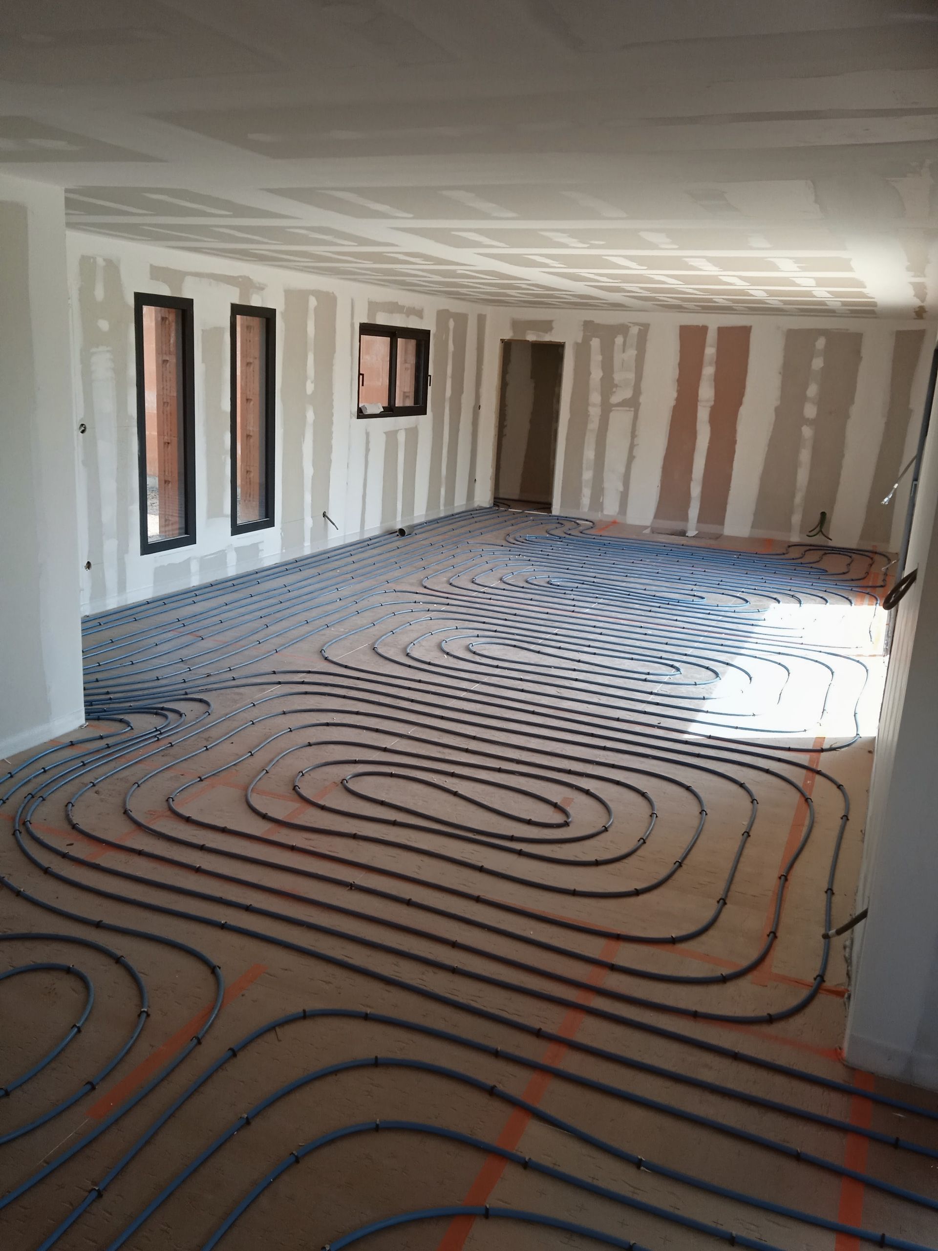 Intérieur en travaux avec des tubes de chauffage au sol radiant installés dans une pièce inachevée.