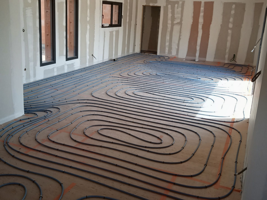Pièce intérieure en construction avec des tubes de chauffage au sol noirs posés sur des panneaux isolants