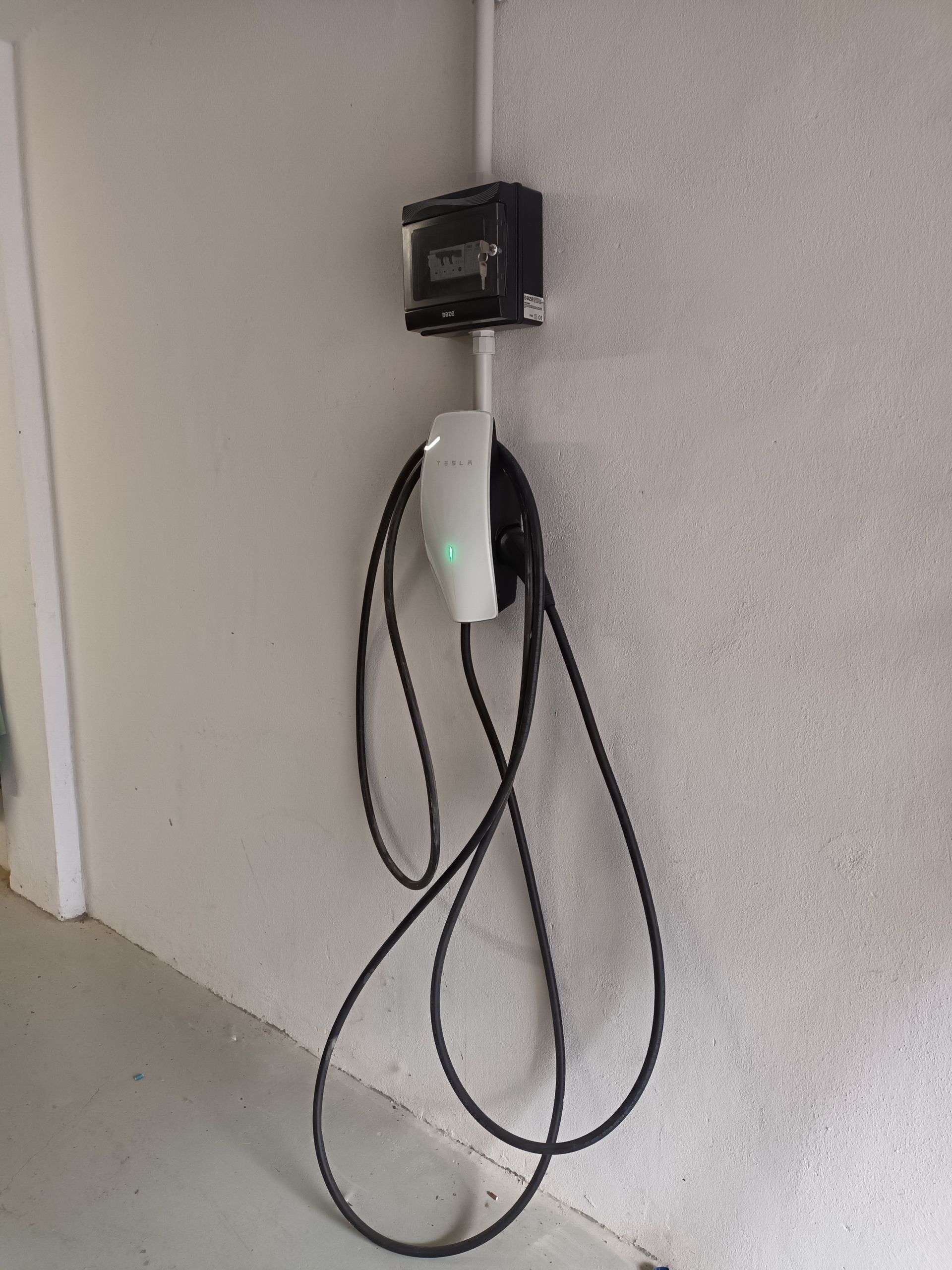 Un cargador de vehículos eléctricos montado en una pared gris claro con un cable negro colgando.