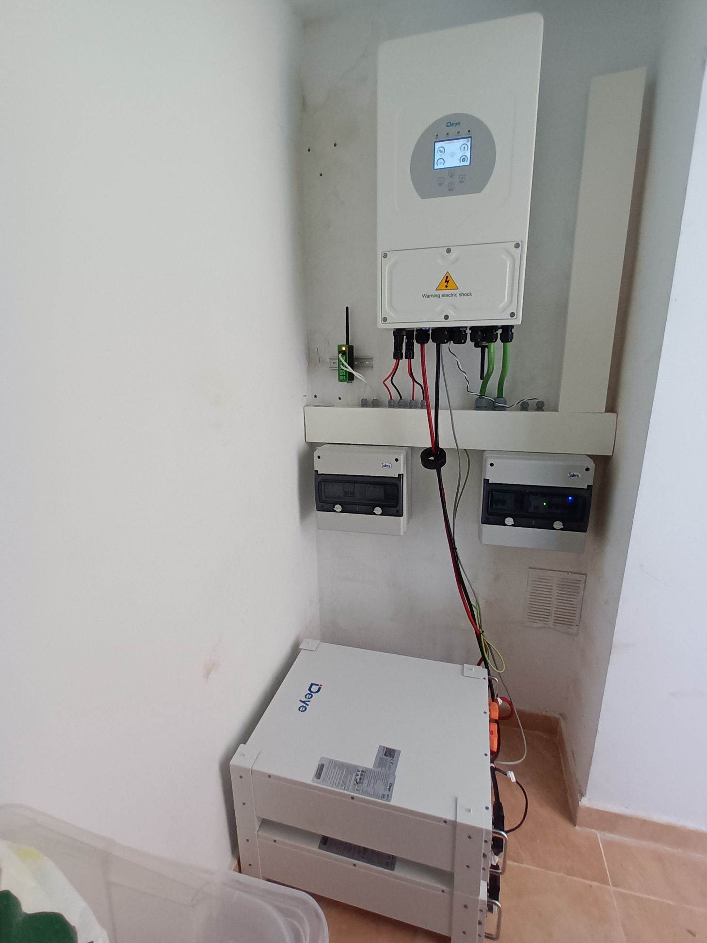 Inversor solar, baterías y disyuntores instalados en una habitación de paredes blancas, probablemente para un sistema de energía doméstica.