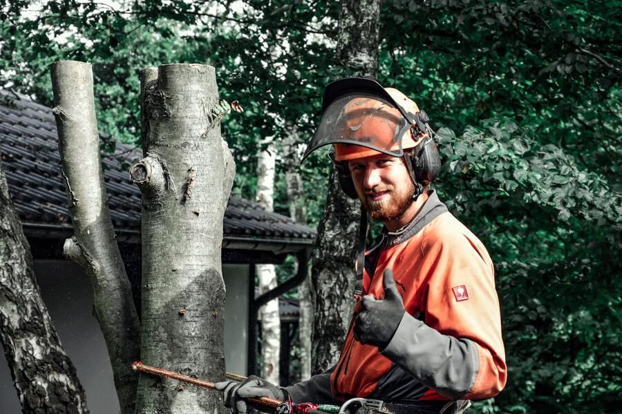 Ein Mann mit Helm und Handschuhen steht neben einem Baum und streckt seinen Daumen nach oben.