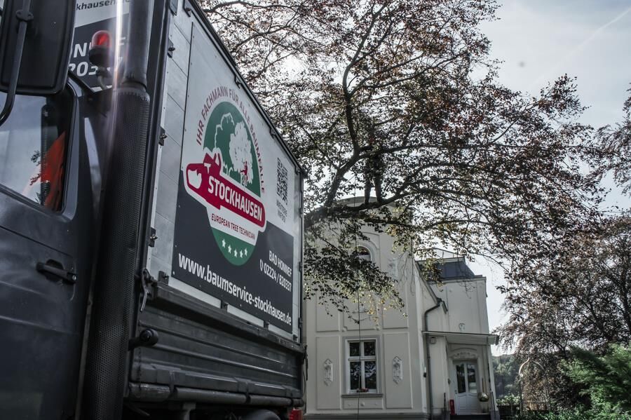 Ein LKW ist vor einem Haus geparkt, im Hintergrund sind Bäume zu sehen.
