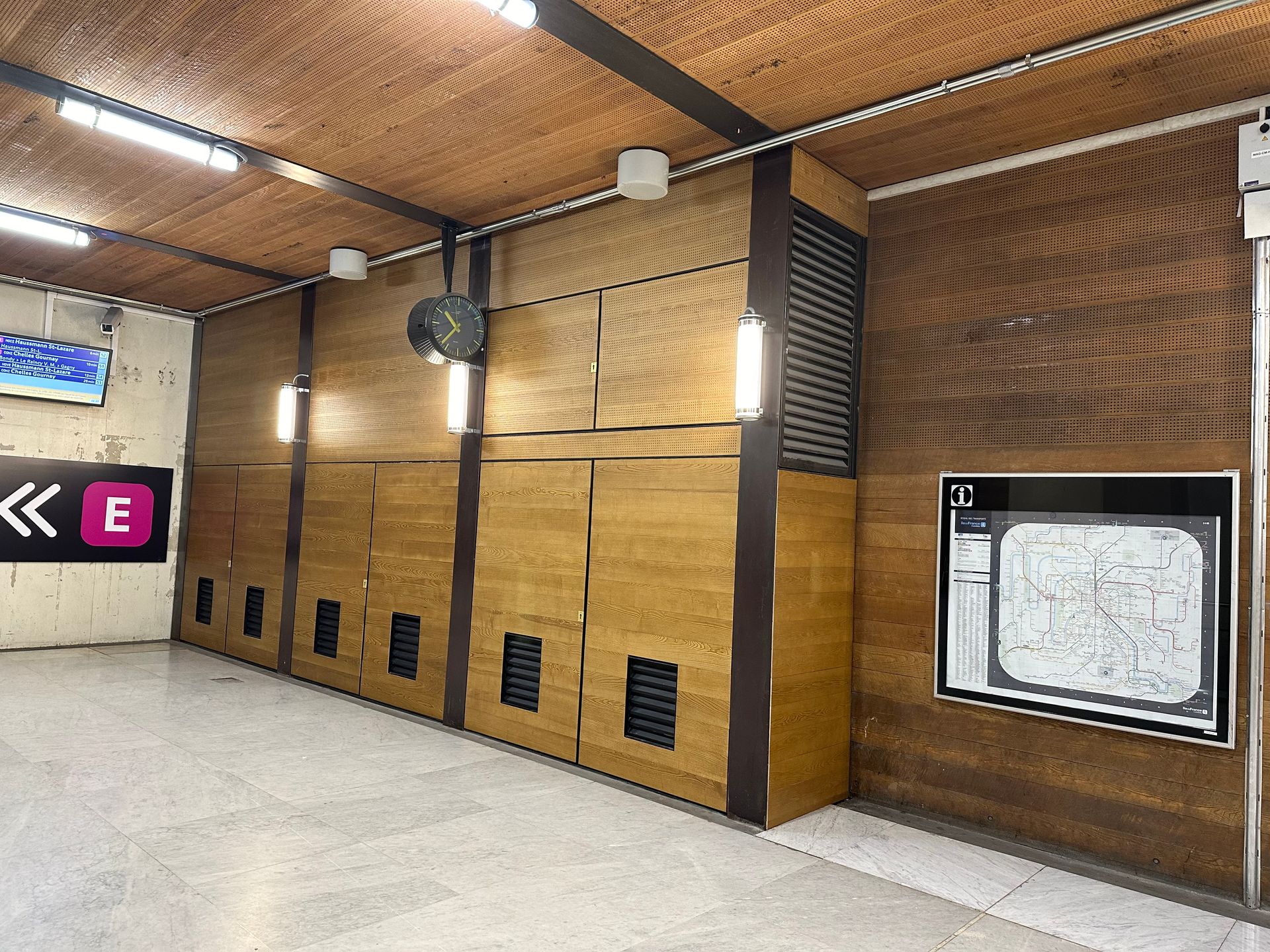 Couloir vide d'une station de métro, avec murs lambrissés, sol carrelé et un plan du réseau sur la droite.