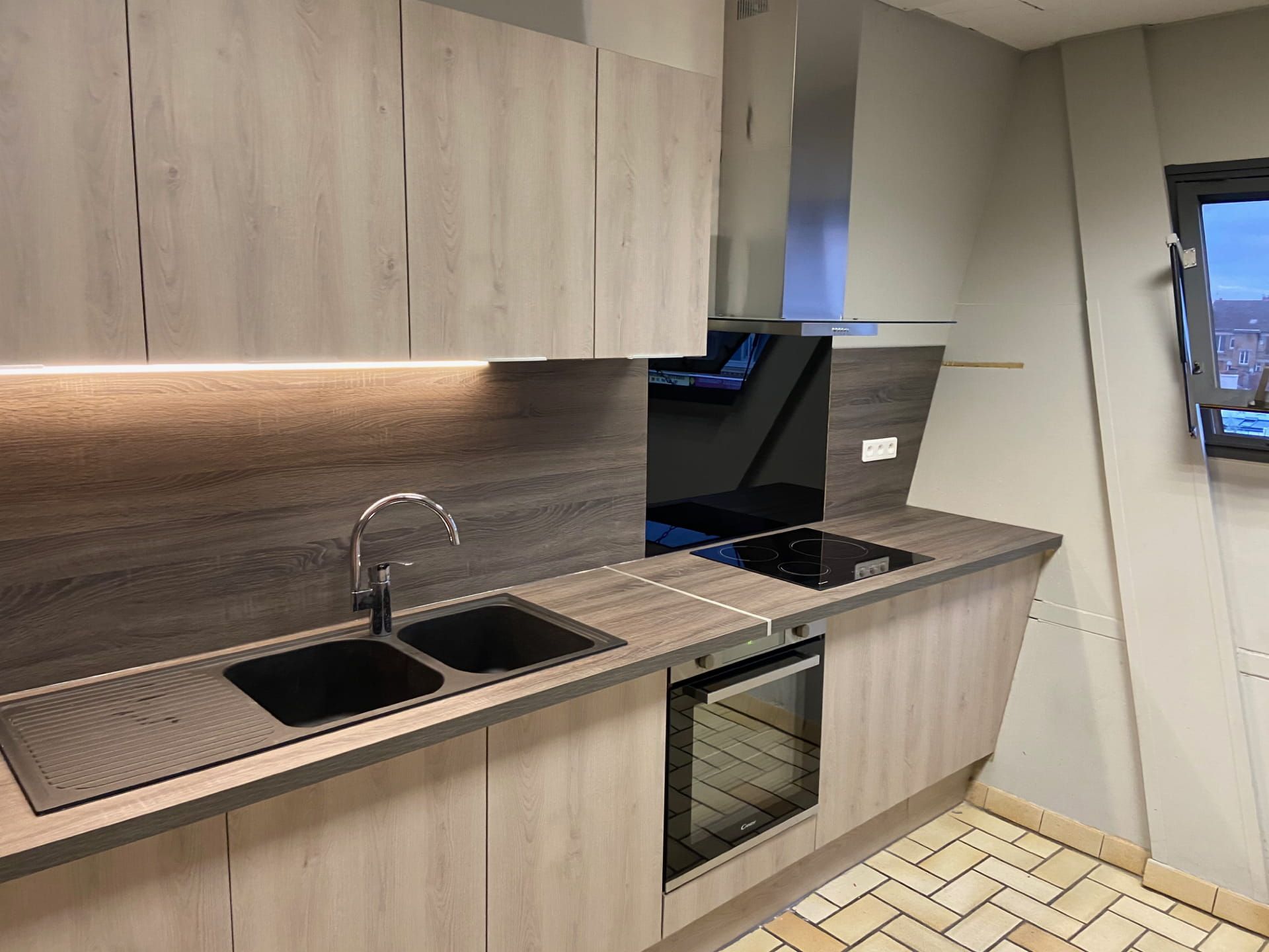 Cuisine moderne avec placards en bois clair, évier, crédence et four encastré.