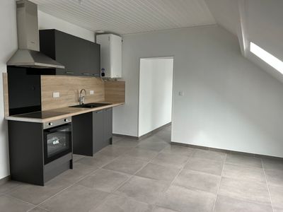 Cuisine mansardée moderne vide avec placards, sol carrelé et murs en pente.