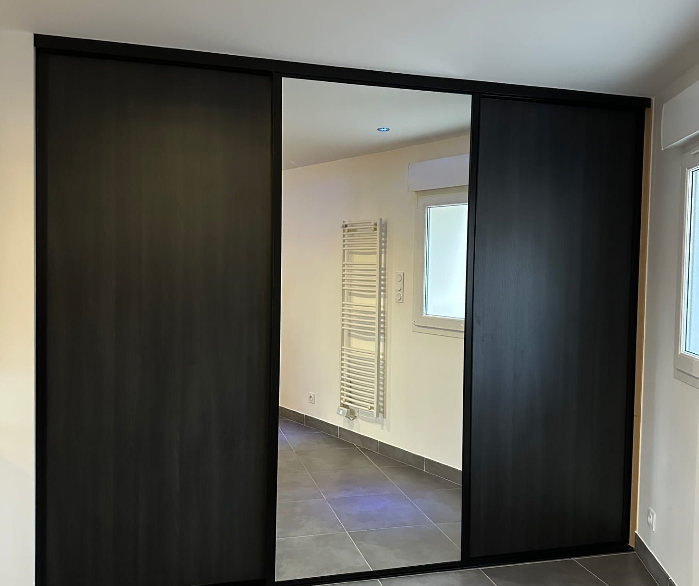 Portes de placard coulissantes avec panneau central miroir dans une pièce lumineuse.