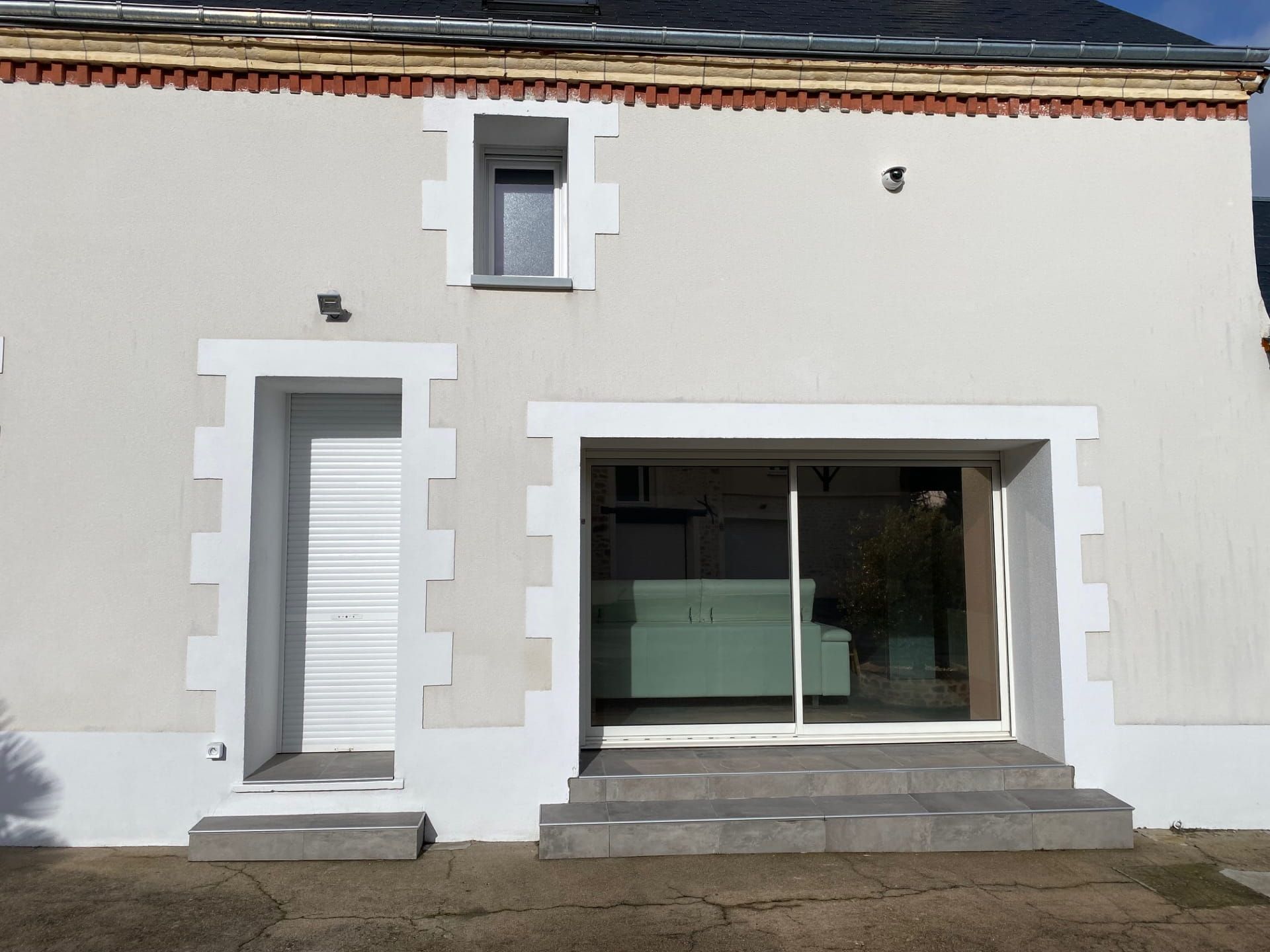 Façade de maison blanche avec une porte d'entrée grise, de grandes portes coulissantes en verre et une petite fenêtre