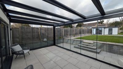 Terrasse couverte avec parois vitrées à cadre, sol carrelé et sièges extérieurs donnant sur une cour arrière.