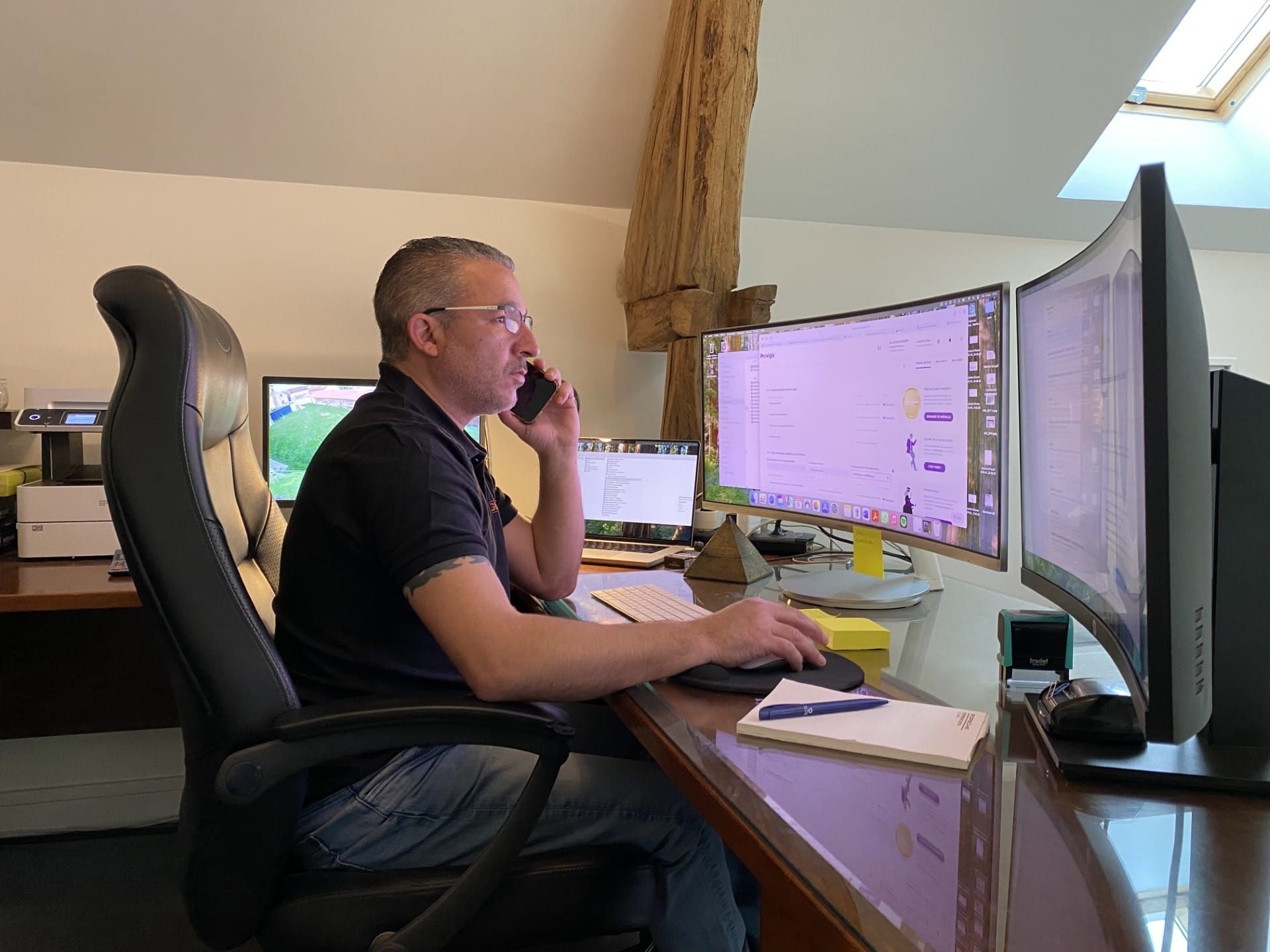 Une personne travaillant à un bureau avec plusieurs écrans, parlant au téléphone dans un espace lumineux