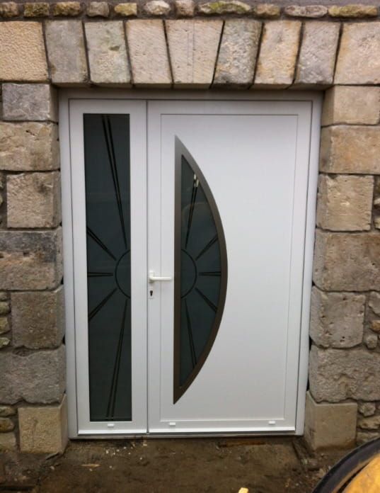 Porte d'entrée avec panneaux de verre foncé encastrés dans un mur en pierre.