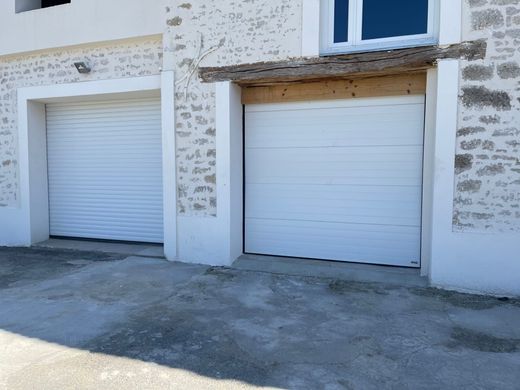 Deux portes de garage fermées sur un bâtiment en pierre avec une allée en béton devant.