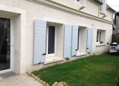 Maison avec volets et pelouse à côté d'une porte-fenêtre.