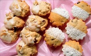 Galletas variadas en una bandeja rosa, algunas rociadas con glaseado y otras espolvoreadas con azúcar glas.