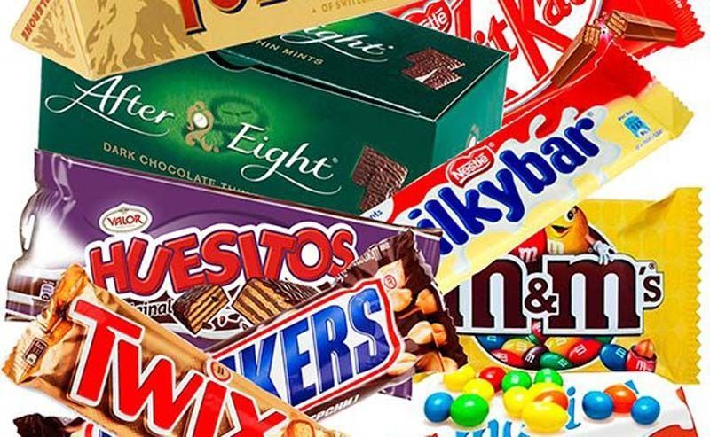 Surtido de barras de chocolate y dulces, incluyendo M&Ms, Twix, Snickers, Huesitos y After Eight, en un colorido montón.