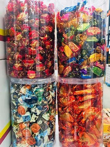 Cuatro recipientes transparentes llenos de caramelos surtidos de colores envueltos.
