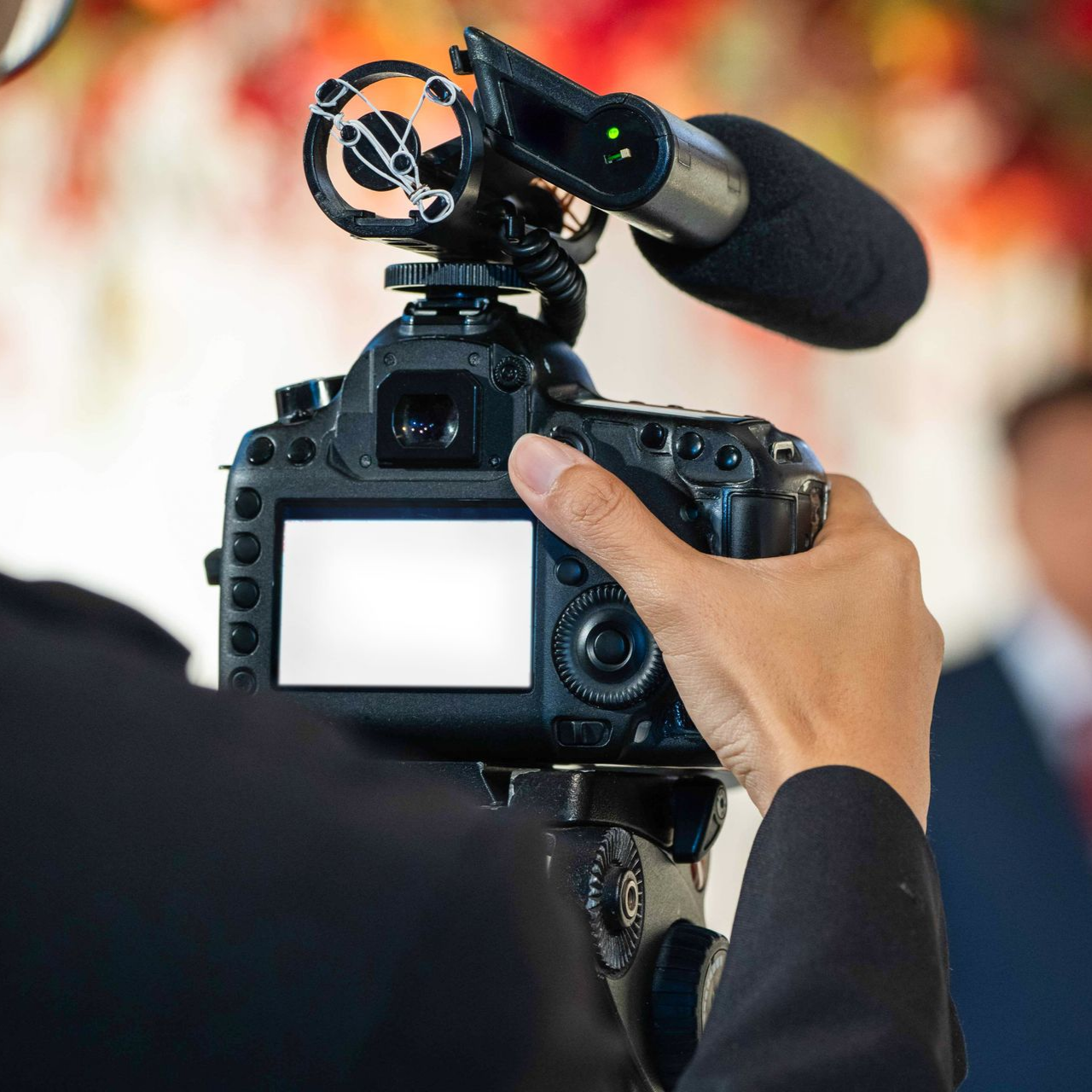 Une personne tient une caméra noire munie d'un microphone et filme.