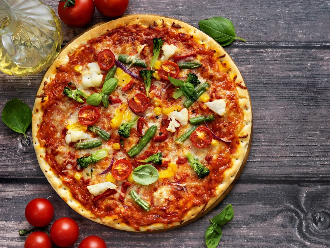 Pizza végétarienne avec sauce tomate, fromage et légumes sur une surface en bois, garnie de tomates et de basilic.