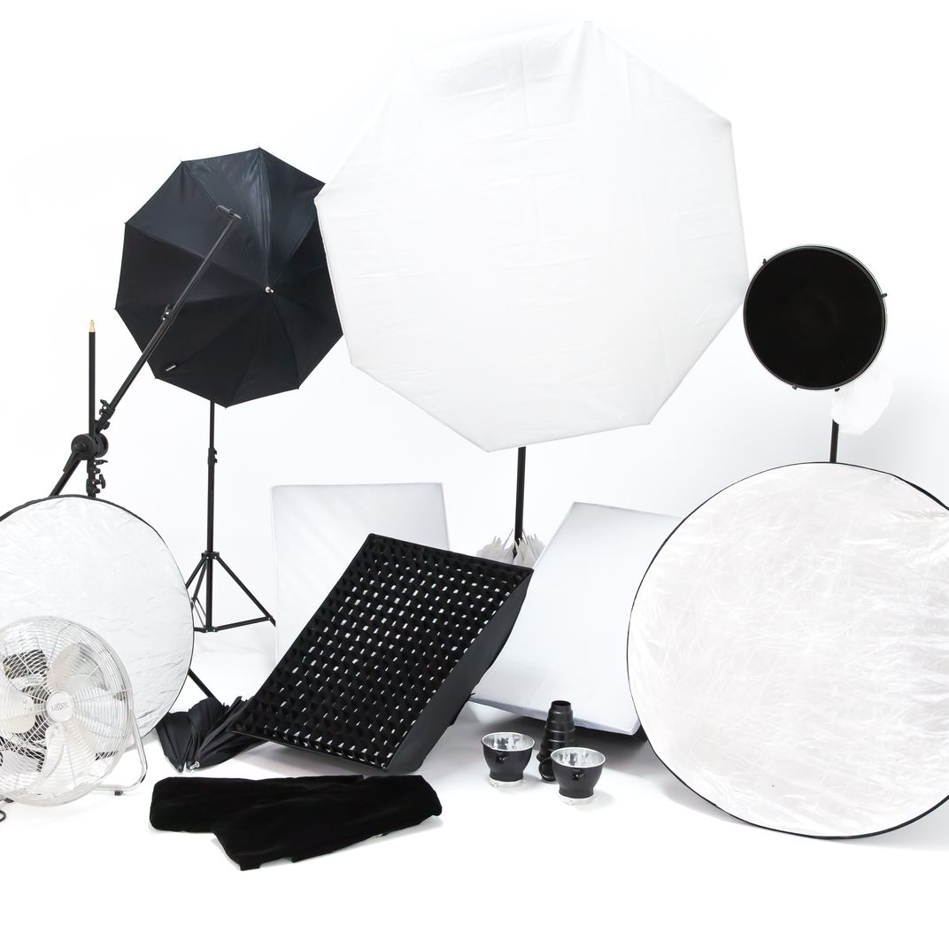 Matériel d'éclairage photographique, comprenant des boîtes à lumière, des parapluies, des réflecteurs et une grille nid d'abeille. Fond blanc.