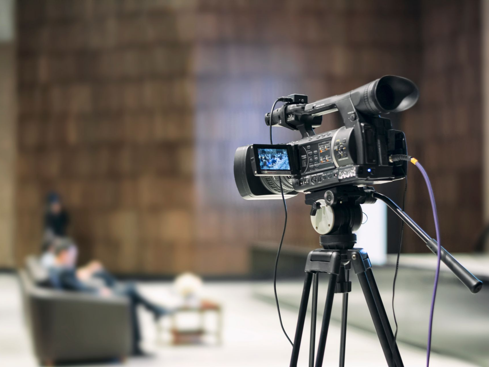 Caméra vidéo sur trépied filmant un intérieur moderne, arrière-plan flou.