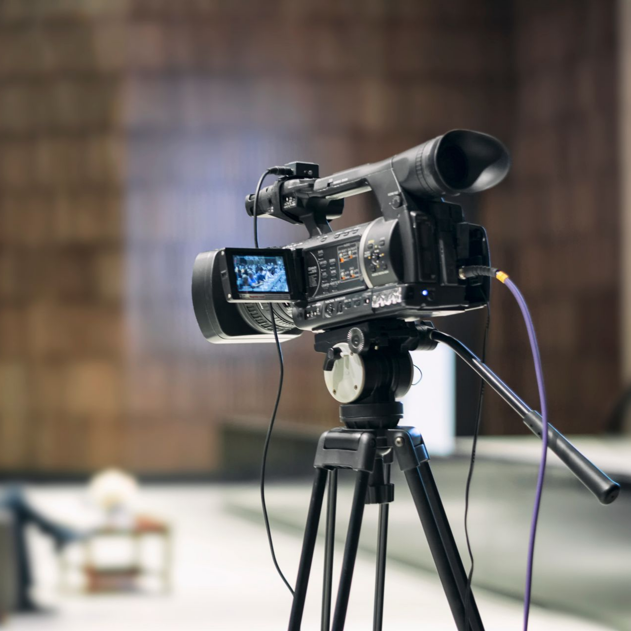 Une caméra vidéo sur trépied filmant dans un décor intérieur flou.