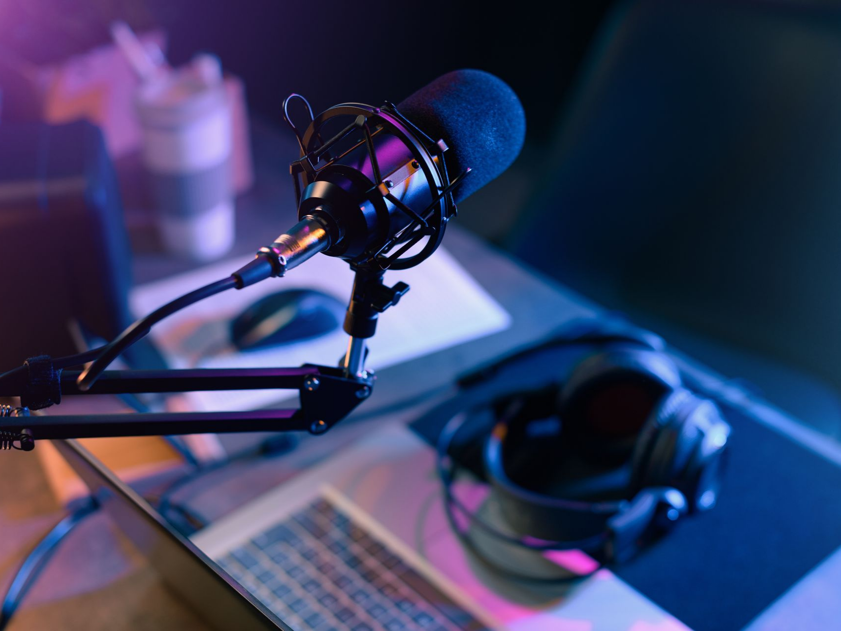 Microphone sur bras articulé, casque et ordinateur portable sur un bureau. Ambiance sombre, éclairage bleu et violet.