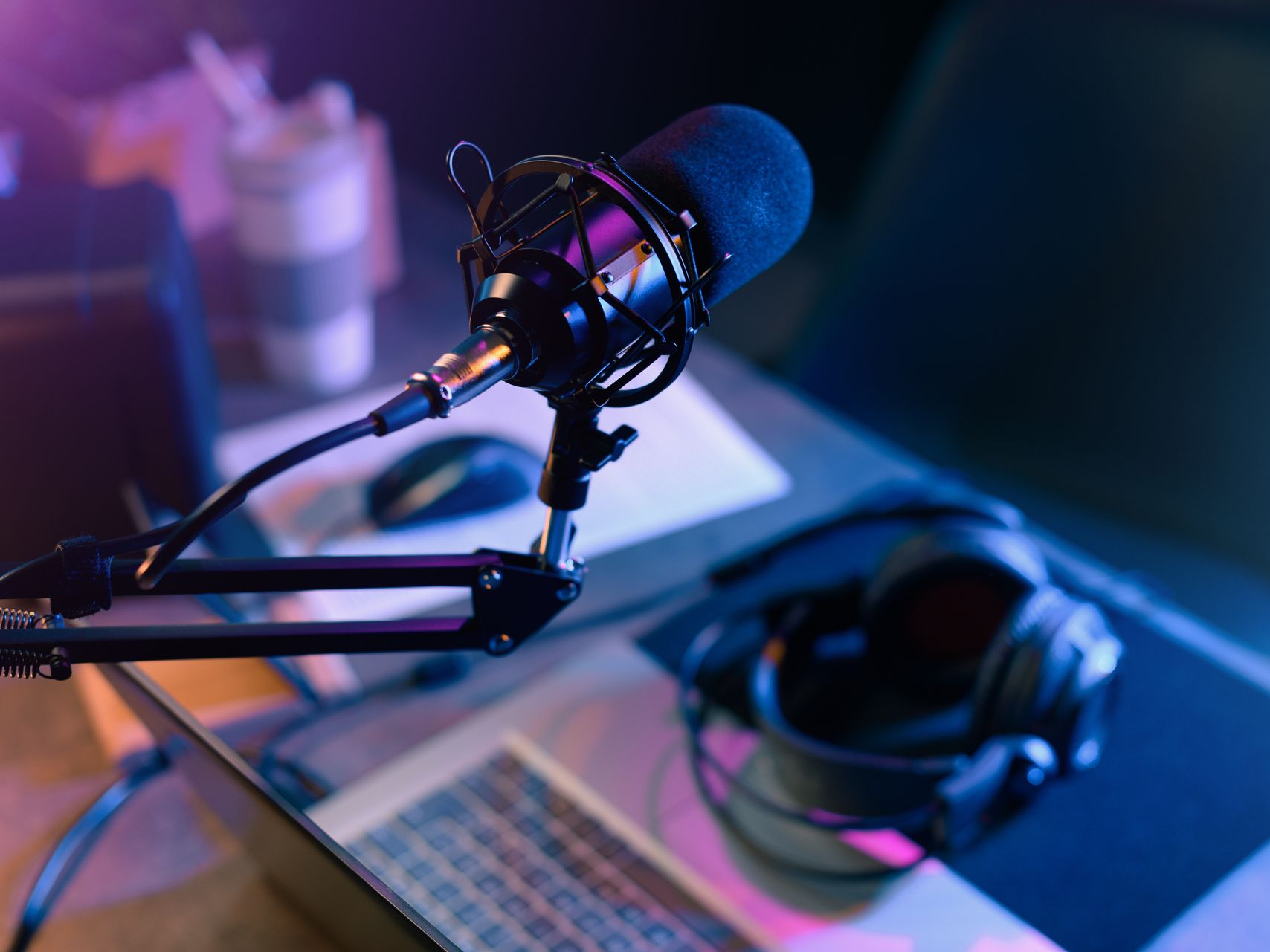 Microphone sur le bureau, casque, ordinateur portable ; configuration d'enregistrement de podcast, éclairage bleu et violet.