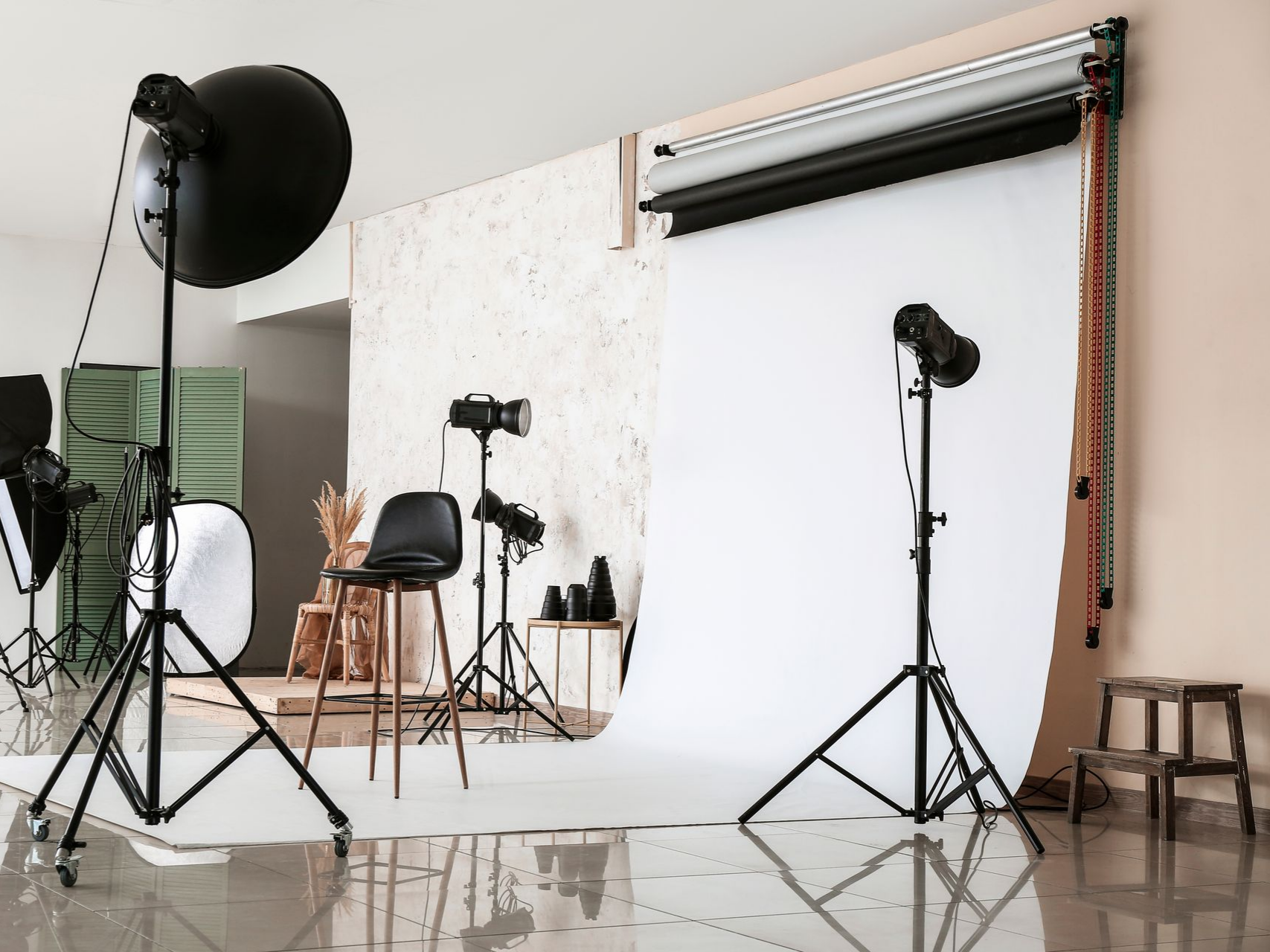 Intérieur d'un studio photo avec équipement d'éclairage, fond blanc et petit tabouret.