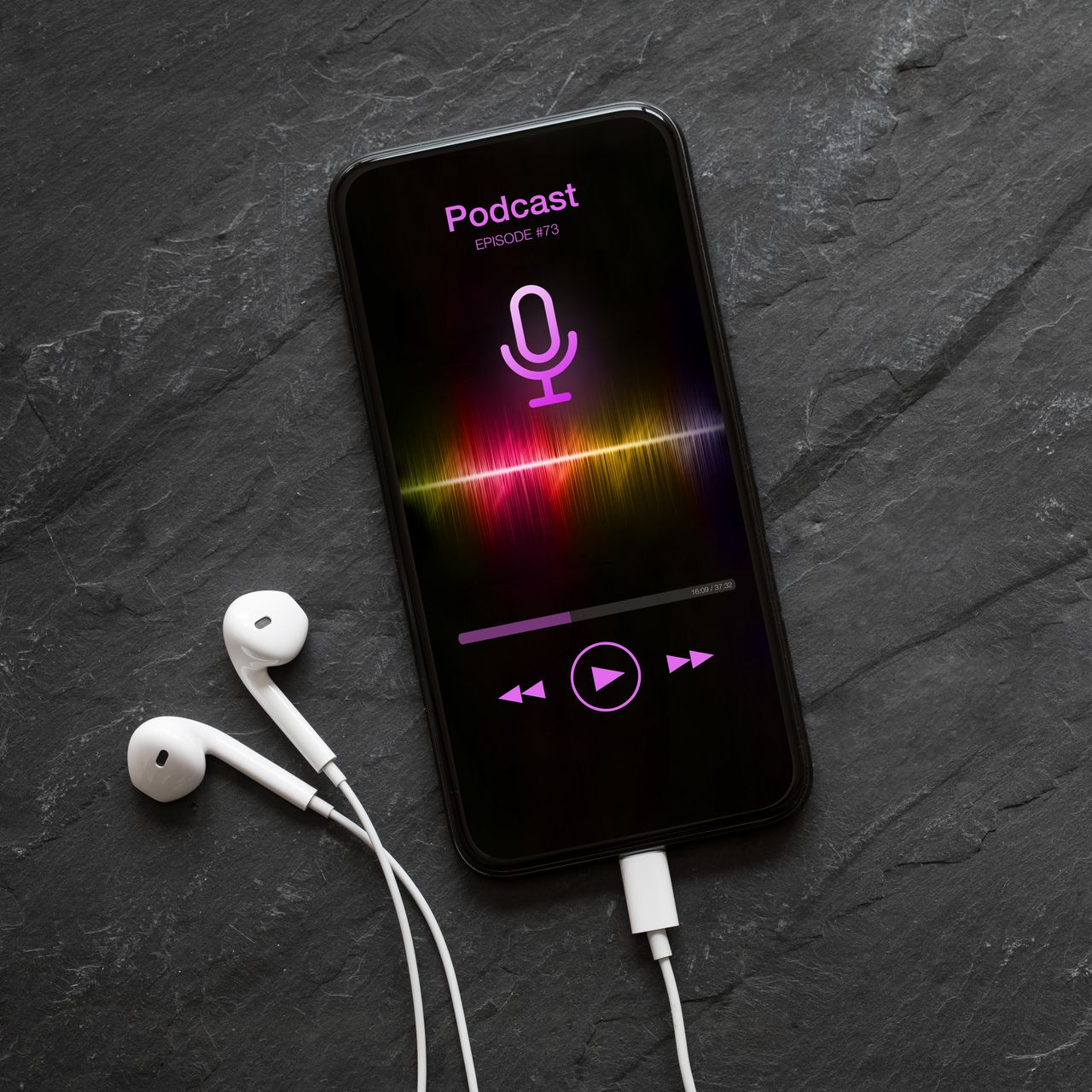 Un smartphone diffuse un podcast, des écouteurs et un câble de chargement sont posés sur une surface sombre.